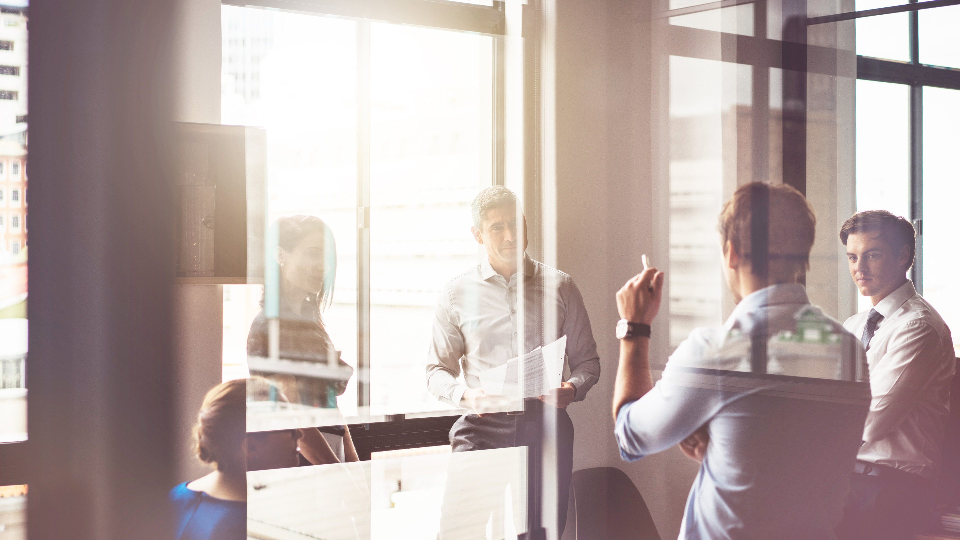 A photo of business people having discussion in board room. Male and female professionals are seen through glass. They are working in office.